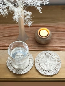 Detail of handmade boho macramé coaster with cotton fringe on a cozy wooden table