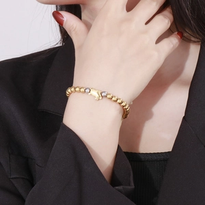 Detail shot of a minimalist gold beaded pig bracelet worn elegantly on a female wrist