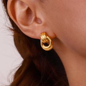Close-up of golden triple interlocking loop earrings shown worn on a model ear