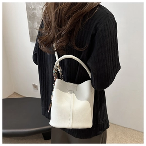 Detail of white bucket bag with lychee pattern, fashion logo, and decorative silk scarf