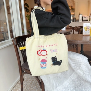 Detail of cute kitten embroidery and milk bottle pattern on beige canvas tote bag