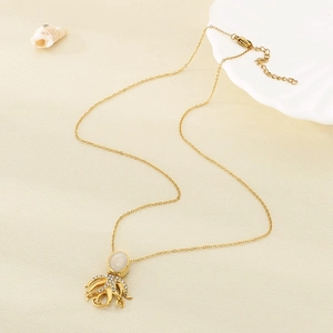 Detail of a golden octopus pendant with white gems and sea shells on a beige background