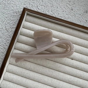 Close-up of beige wave resin hair claw clip displayed on linen tray in soft light