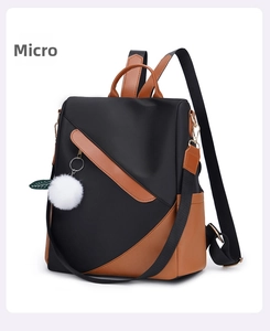 Detail of waterproof nylon backpack with brown leather trim and white pom-pom charm