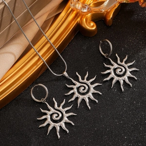 Flat lay of silver sunburst pendant necklace and earrings on a textured black backdrop