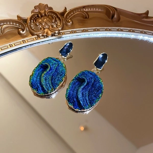Detailed close-up of blue resin earrings on a vintage mirror with golden frames