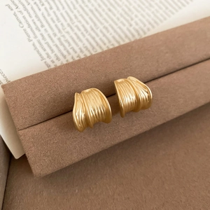 Close-up of golden metal earrings with unique brushed texture on a brown suede stand