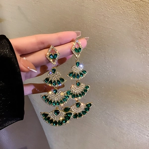 Detail of long gold fan-shaped earrings with green stones and sparkling fringe