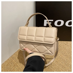 Detail view of beige quilted handbag with crossbody strap and gold-tone magnetic buckle