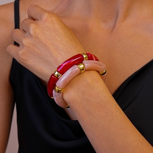 Détail macro de bracelets en acrylique rouge et rose avec perles dorées sur le poignet