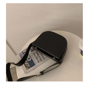 Top view of a black saddle bag with gold hardware on a table with coffee and newspaper