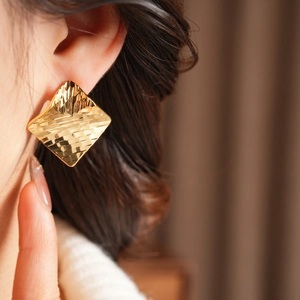 Gros plan de boucles d'oreilles losanges dorées avec texture ondulée portées par un modèle