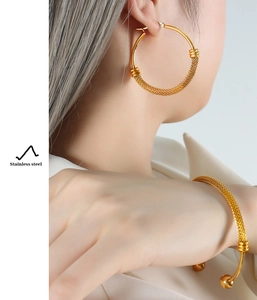 Close-up of golden stainless steel earring and bracelet with fine woven metal texture
