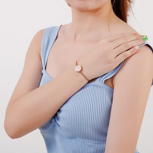 Detailed view of rose gold stainless steel bracelet with cutout logo charm on model's wrist