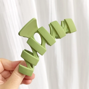 Détail d'une grande pince à cheveux vert mat avec design ondulé sur fond blanc