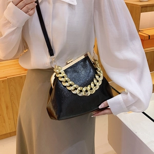 Chic black glossy leather handbag with bold gold chain, shown on model for scale