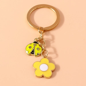 Detail of metal keychain featuring yellow enamel ladybug and flower charms on a gold ring