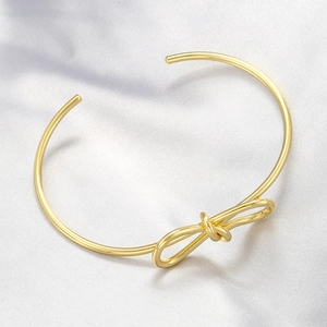 Elegant gold bow cuff bracelet with twisted knot design on white satin background