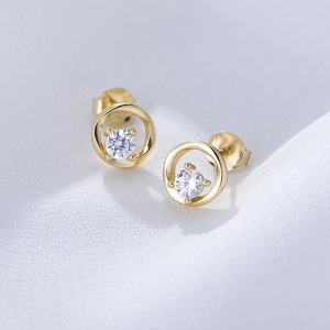 Macro shot of gold hollow round stud earrings with four-prong set white zircon on blue silk