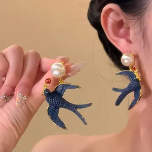 Gros plan détaillé de la boucle d'oreille hirondelle avec perle blanche et fini bleu