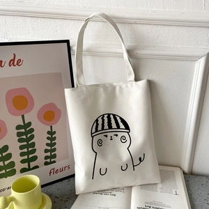 Detail of white canvas tote bag with black cartoon line art in a cozy interior setting