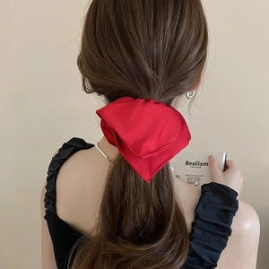 Close-up of a large red satin bow hair tie worn on long brown hair for an elegant look