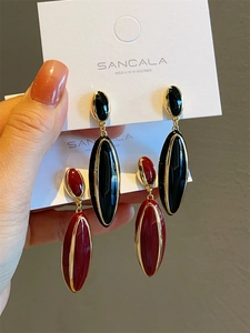 Detailed view of enamel teardrop earrings in black and burgundy with gold trim