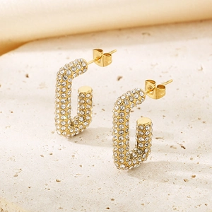 Détail de boucles d'oreilles ovales en U dorées avec cristaux pavés sur fond de pierre beige