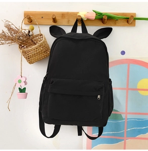 Detail of a black canvas backpack with cute rabbit ears hanging on a wooden wall hook