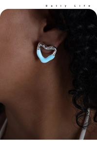 Close-up of heart-shaped blue enamel stud earrings worn by a model in daily life