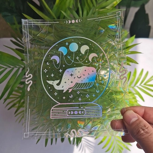 Rainbow suncatcher window cling with whale and moon phases held against green leaves