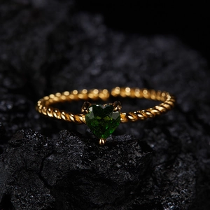 Macro detail of a twisted gold ring with a green heart gemstone on black volcanic rock