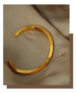 Detailed close-up of a gold-plated twisted cuff bangle on elegant champagne silk fabric