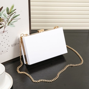 Elegant white acrylic clutch box bag with gold metal chain strap on a wooden desk
