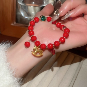 Macro detail of red glass bead bracelet with golden rocking horse and green gem charm