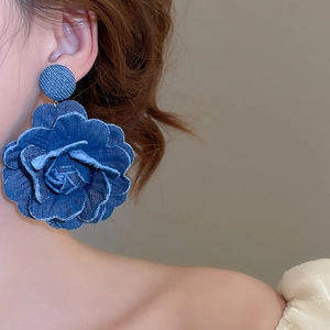 Detailed close-up of large blue denim fabric flower earrings with textured raw edges