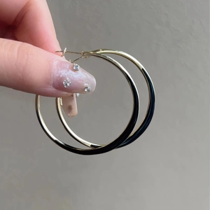 Detail view of large gold and black enamel hoop earrings held by hand on neutral backdrop