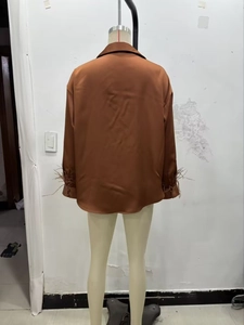 Detail view of brown satin blouse featuring elegant feather trim on the long sleeves
