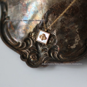 Detail of square white shell necklace with gold bee pendant on vintage metal surface
