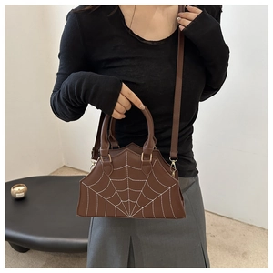 Detail of brown spiderweb embroidery and golden hardware on fashionable handbag