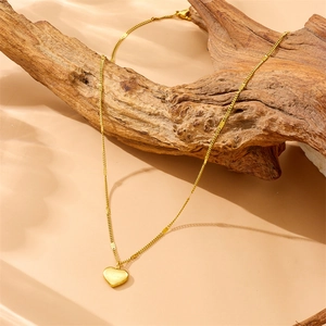 Gold-plated stainless steel necklace with heart pendant draped on a wooden branch