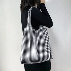 Close-up of a black and white checkered canvas tote bag worn over the shoulder by a model