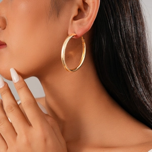 Close-up of a large polished gold hoop earring worn by a model in a fashion setting