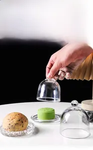 Close-up of a hand lifting a crystal glass dome lid from a small dessert platter