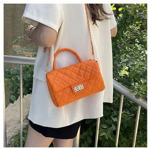 Close-up of orange quilted chain bag with gold diamond lock and metallic handle