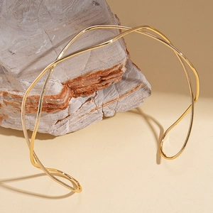 Detailed view of elegant wavy gold metal choker on a textured stone background