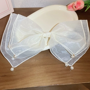 Detail of white organza bow hair clip with elegant pearl tassel on a vintage tray