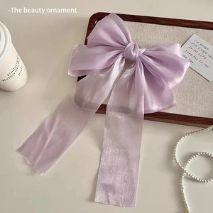 Detail view of a large purple organza bow hair clip styled in a luxury cream tray