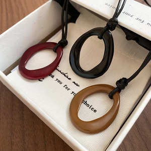 Trois colliers minimalistes en résine rouge, noir et marron dans une boîte cadeau