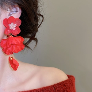 Detailed view of red floral drop earrings with layered petals and beads on a model